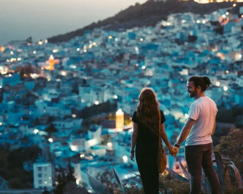 A romantic couple holding hands with a view of Chefchaouen, Morocco at twilight.